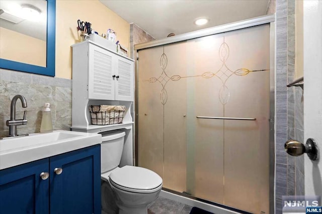 bathroom with vanity, a shower with shower door, tile walls, and toilet