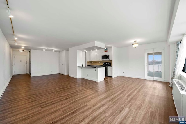 unfurnished living room featuring radiator, hardwood / wood-style floors, and rail lighting