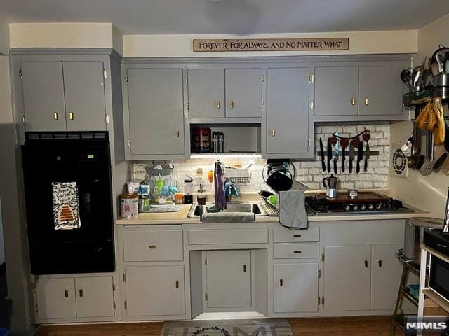 kitchen with decorative backsplash, stainless steel gas cooktop, sink, gray cabinets, and black oven