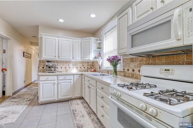 kitchen with white appliances, sink, tasteful backsplash, light tile patterned flooring, and white cabinetry