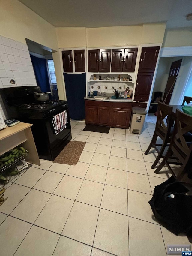 kitchen featuring decorative backsplash, dark brown cabinets, light tile patterned floors, and black gas range oven