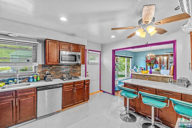 kitchen with sink, backsplash, decorative light fixtures, ceiling fan with notable chandelier, and appliances with stainless steel finishes