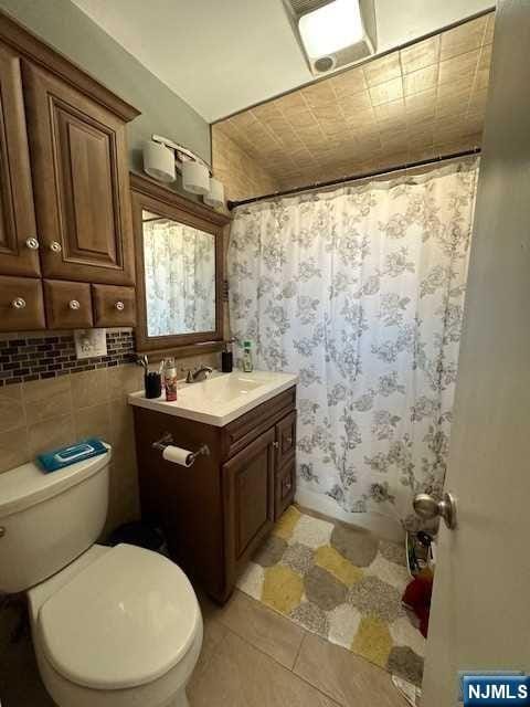 bathroom featuring walk in shower, tile patterned floors, toilet, vanity, and tile walls