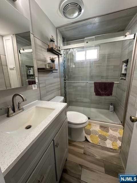 bathroom featuring wood-type flooring, vanity, toilet, and walk in shower