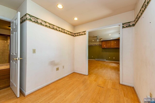 interior space with ceiling fan, a baseboard heating unit, and light wood-type flooring