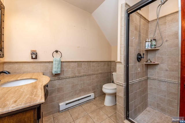 bathroom featuring tile patterned flooring, a baseboard heating unit, toilet, vanity, and tile walls