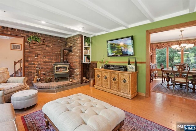 living room with a wood stove, an inviting chandelier, wood-type flooring, and beamed ceiling