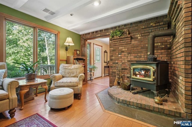 sitting room featuring wood-type flooring, a wood stove, beamed ceiling, and brick wall