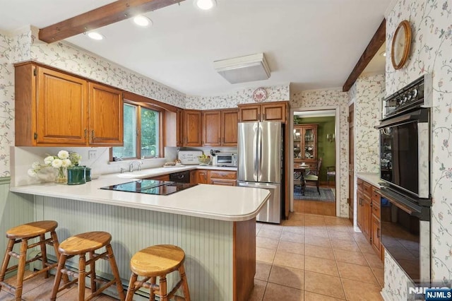 kitchen with beamed ceiling, a breakfast bar, black appliances, and kitchen peninsula