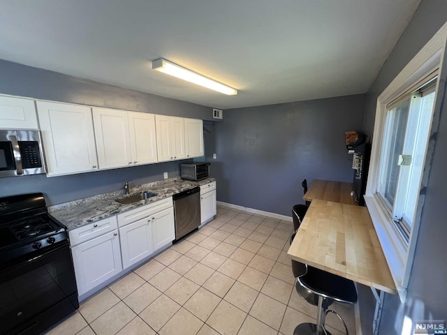 kitchen featuring light stone counters, stainless steel appliances, sink, light tile patterned floors, and white cabinetry