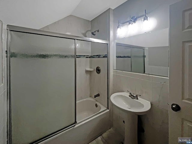bathroom with vaulted ceiling, sink, enclosed tub / shower combo, and tile walls