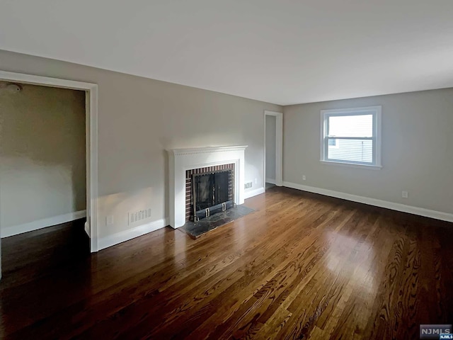 unfurnished living room with dark hardwood / wood-style flooring and a brick fireplace