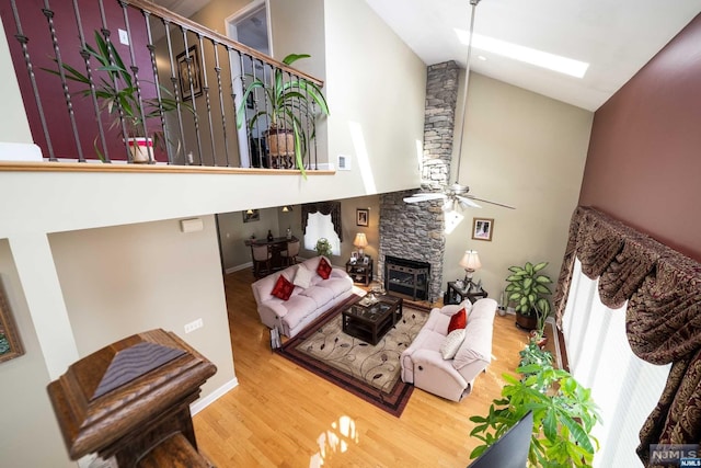 living room with a fireplace, hardwood / wood-style flooring, lofted ceiling with skylight, and ceiling fan