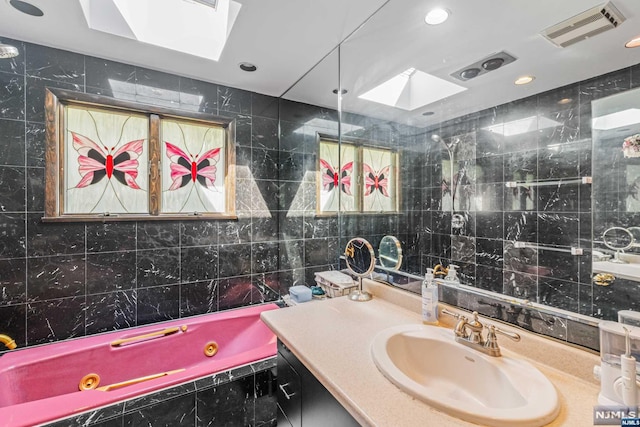 bathroom with a skylight, vanity, a relaxing tiled tub, and tile walls