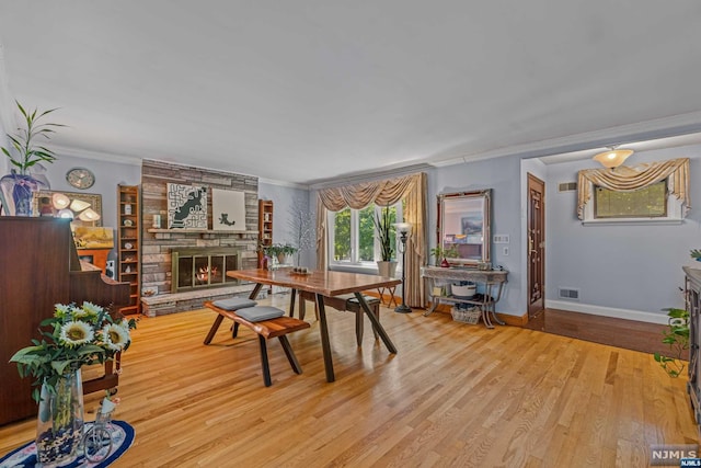 dining space with a large fireplace, light wood-type flooring, and crown molding