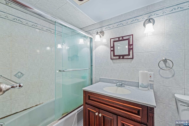 full bathroom featuring shower / bath combination with glass door, vanity, tile walls, and toilet