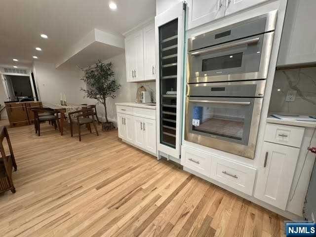 kitchen featuring light hardwood / wood-style floors, white cabinetry, stainless steel double oven, and tasteful backsplash