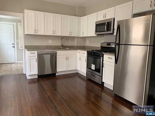 kitchen featuring stainless steel appliances, sink, stone counters, dark hardwood / wood-style floors, and white cabinetry