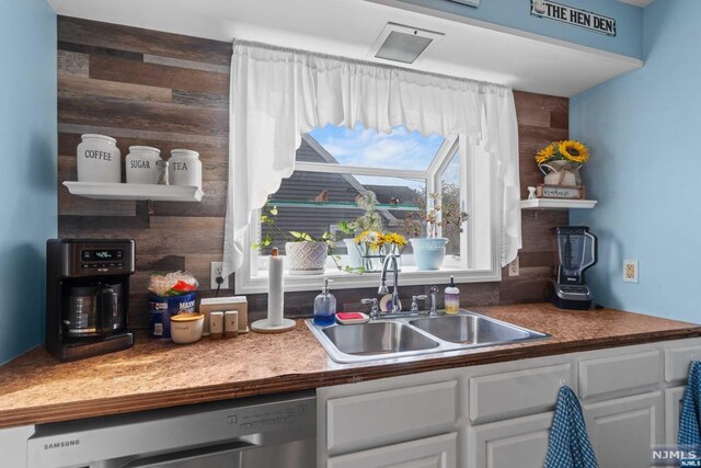 kitchen featuring dishwasher, white cabinetry, sink, and wooden walls