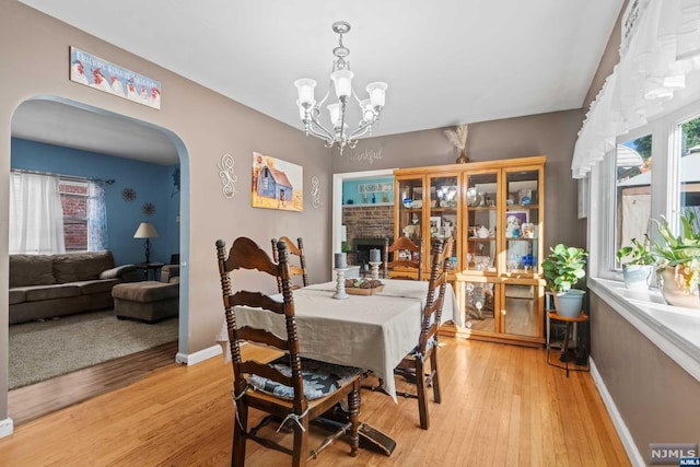 dining room with a brick fireplace, a chandelier, and light hardwood / wood-style flooring