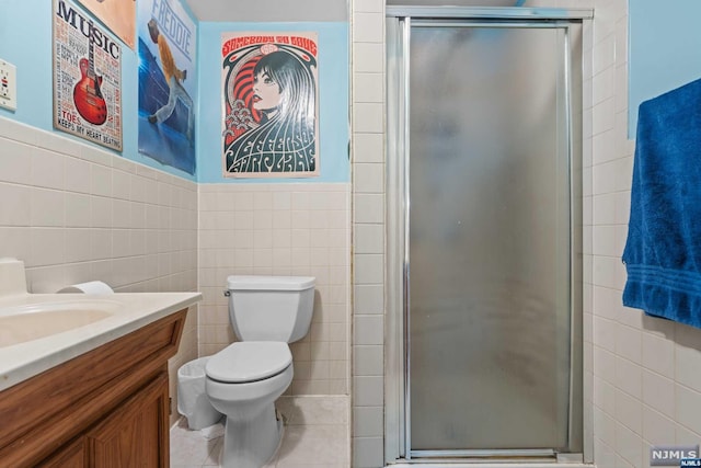 bathroom with tile patterned floors, vanity, a shower with door, tile walls, and toilet