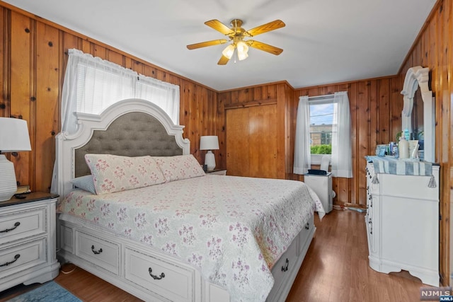 bedroom featuring ceiling fan, wood-type flooring, and wooden walls