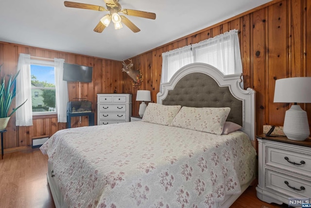 bedroom featuring baseboard heating, ceiling fan, wood walls, and light wood-type flooring