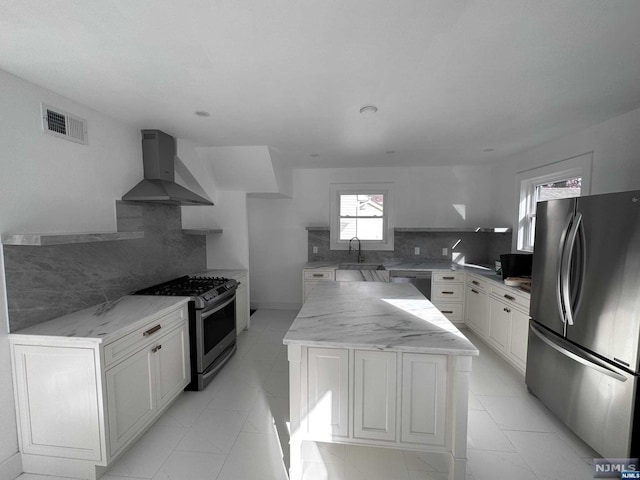 kitchen featuring backsplash, wall chimney range hood, a center island, stainless steel appliances, and white cabinets