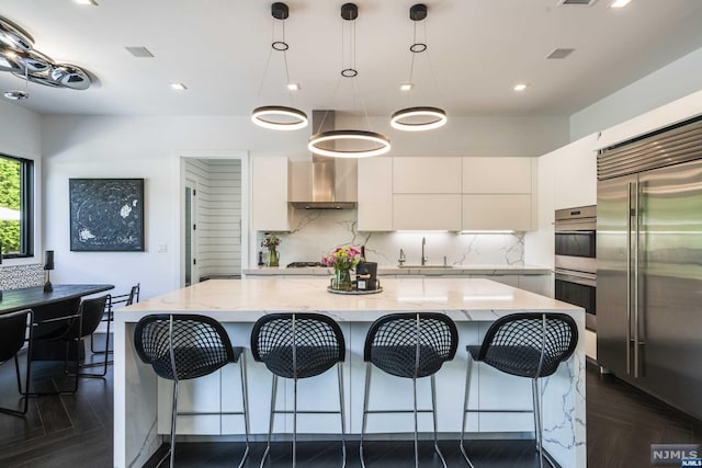 kitchen with appliances with stainless steel finishes, wall chimney exhaust hood, pendant lighting, white cabinets, and a kitchen island