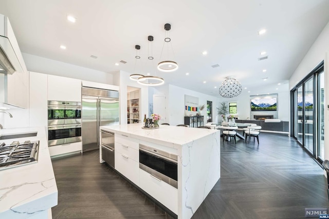 kitchen featuring white cabinets, a spacious island, sink, appliances with stainless steel finishes, and decorative light fixtures