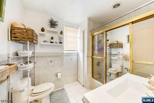 full bathroom featuring combined bath / shower with glass door, tile patterned floors, tile walls, and toilet