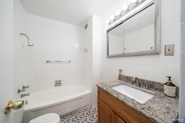 full bathroom featuring vanity, tiled shower / bath, tile walls, and toilet