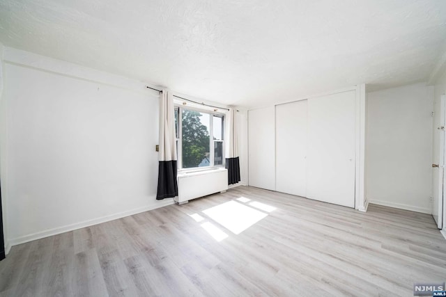 interior space featuring light hardwood / wood-style floors, radiator heating unit, a textured ceiling, and a closet