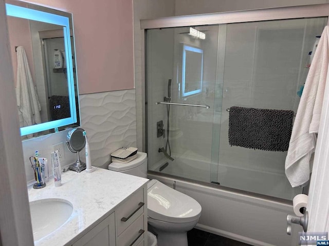 full bathroom with combined bath / shower with glass door, tile patterned floors, toilet, vanity, and tile walls