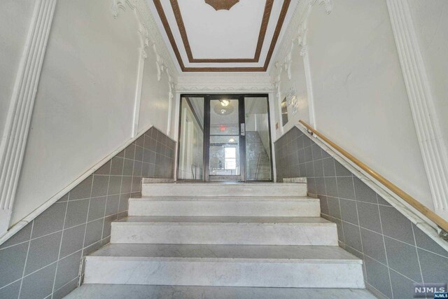 stairs featuring tile walls and crown molding