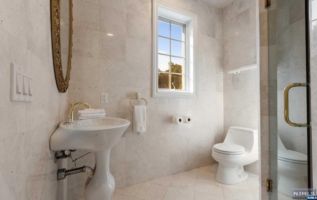 bathroom with tile patterned floors, a shower with door, tile walls, and toilet