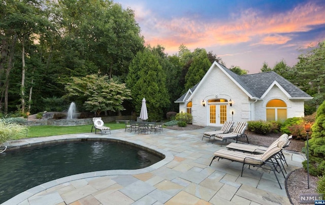 pool at dusk with french doors, a patio area, and an outdoor structure