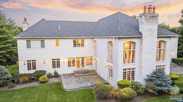 back house at dusk with french doors, a yard, and a patio area