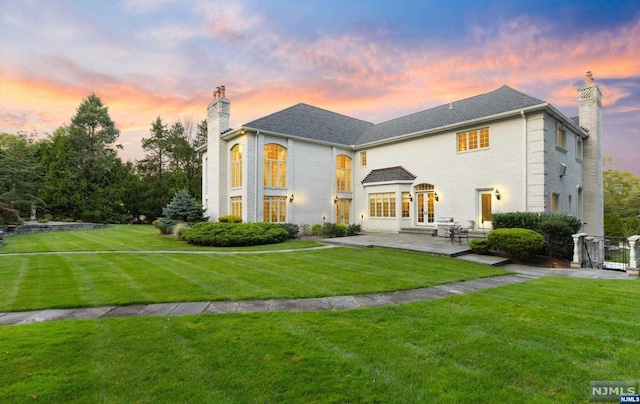 back house at dusk with a lawn, a patio area, and french doors