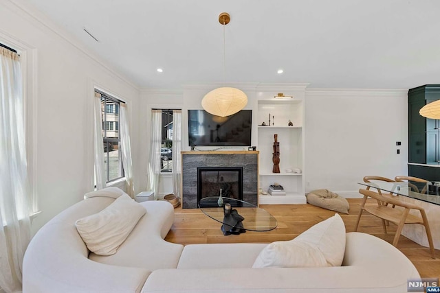 living room featuring built in shelves, ornamental molding, and light wood-type flooring