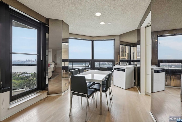 dining room with washer and clothes dryer, light hardwood / wood-style flooring, a water view, and a textured ceiling