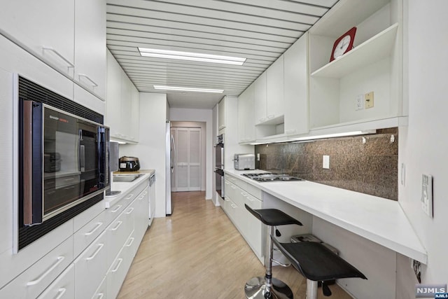 kitchen featuring tasteful backsplash, white cabinets, stainless steel appliances, and light hardwood / wood-style floors