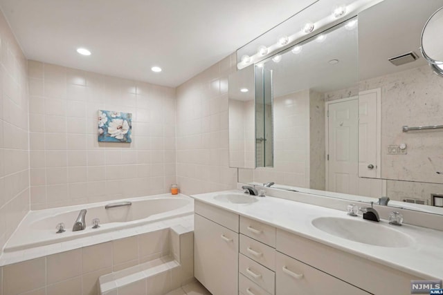 bathroom featuring vanity, a relaxing tiled tub, and tile walls