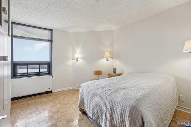 bedroom featuring radiator heating unit, a textured ceiling, and light parquet floors