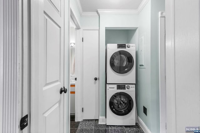 laundry room featuring dark tile patterned floors, stacked washing maching and dryer, and ornamental molding