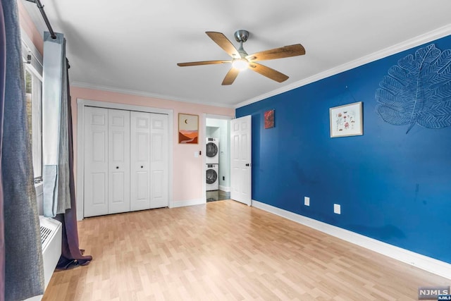 unfurnished bedroom with light hardwood / wood-style flooring, ceiling fan, ornamental molding, stacked washer / drying machine, and a closet