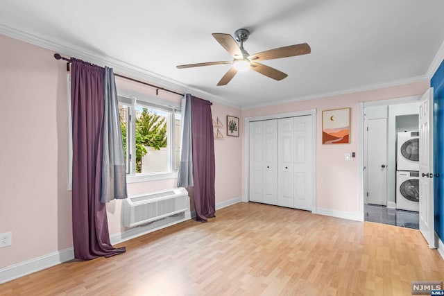 unfurnished bedroom featuring a wall mounted air conditioner, light wood-type flooring, ceiling fan, and stacked washer / drying machine