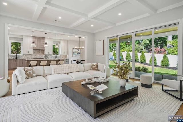 living room with sink, beamed ceiling, a chandelier, and coffered ceiling