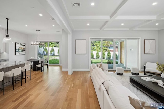 living room with plenty of natural light, beamed ceiling, a chandelier, and light wood-type flooring