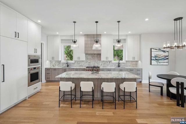 kitchen with decorative light fixtures, white cabinetry, a large island, and sink